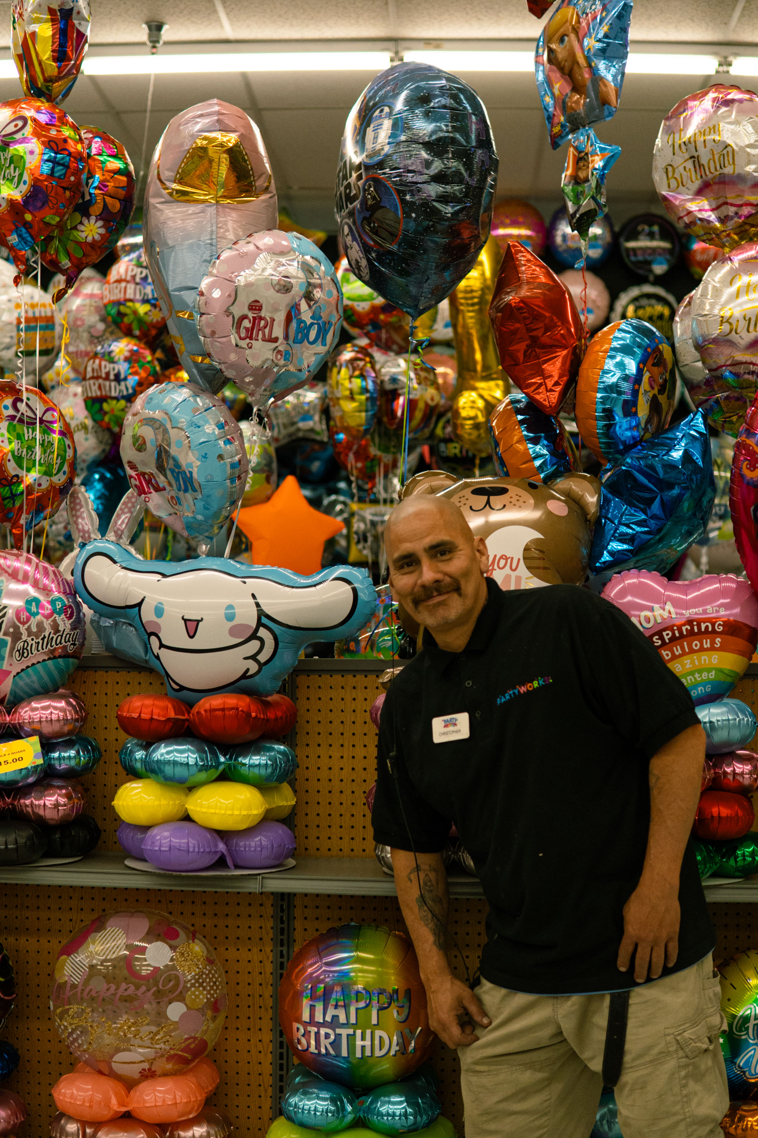 PartyWorks team member smiling in branded polo in front of balloon wall